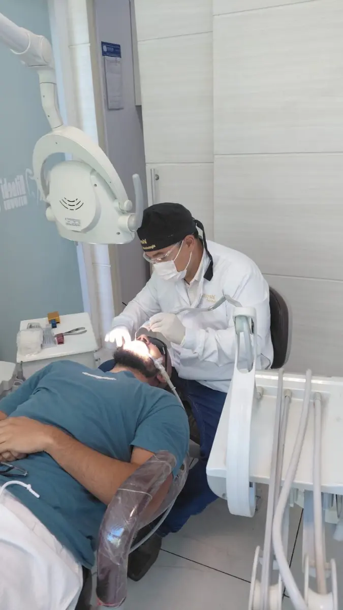 Profissional dentista da Hitoshi Odontologia realizando atendimento clínico em um paciente na cadeira odontológica, em consultório equipado na cidade de Belo Horizonte.